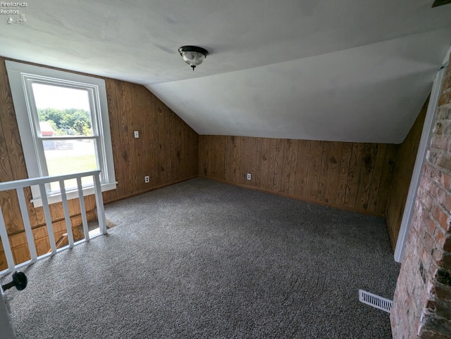 additional living space with carpet flooring, wooden walls, lofted ceiling, and brick wall