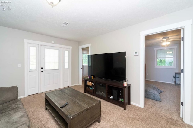 carpeted living room with a textured ceiling, ceiling fan, and a wealth of natural light