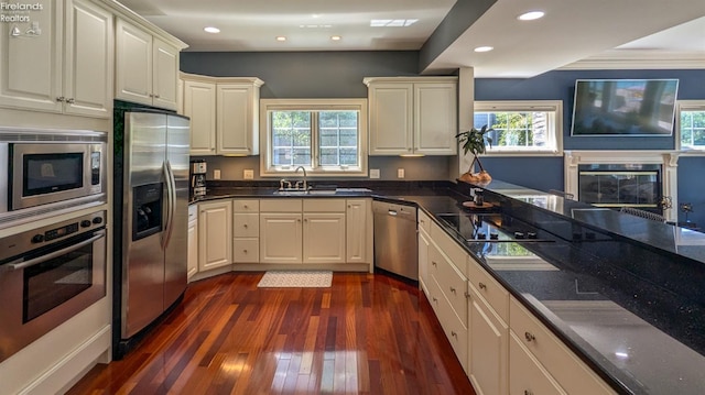 kitchen featuring sink, dark stone countertops, dark hardwood / wood-style floors, stainless steel appliances, and a fireplace