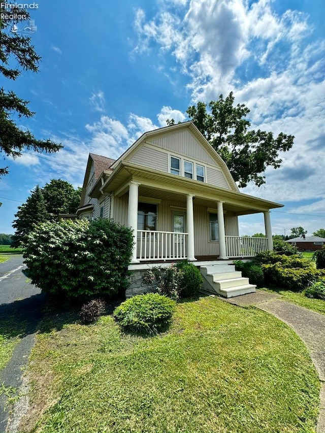 view of front of property with driveway, a porch, a front yard, and a gambrel roof