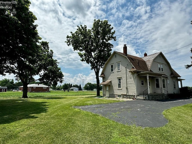 view of side of property with aphalt driveway, roof with shingles, a yard, a chimney, and a gambrel roof