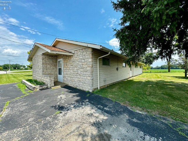 view of side of home featuring a yard, aphalt driveway, and stone siding