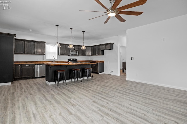 kitchen featuring light hardwood / wood-style flooring, wood counters, ceiling fan, appliances with stainless steel finishes, and a breakfast bar area