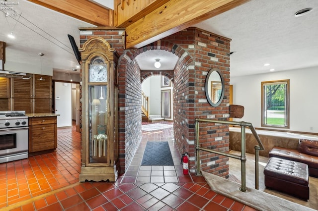 interior space with a textured ceiling, brick wall, beamed ceiling, dark tile patterned floors, and white gas stove