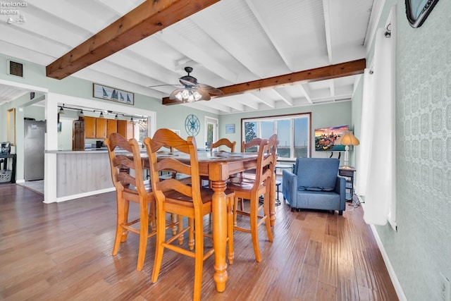 dining area featuring dark wood-type flooring, ceiling fan, a barn door, and beamed ceiling