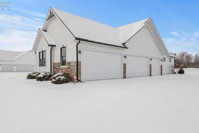 view of snow covered exterior with stone siding, board and batten siding, and an attached garage