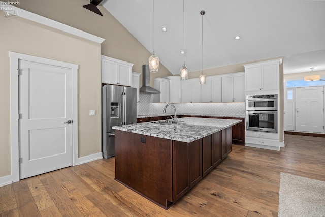 kitchen featuring white cabinetry, stainless steel appliances, wall chimney range hood, and wood finished floors