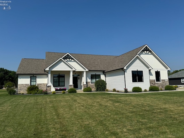 view of front facade with stone siding, a shingled roof, and a front yard