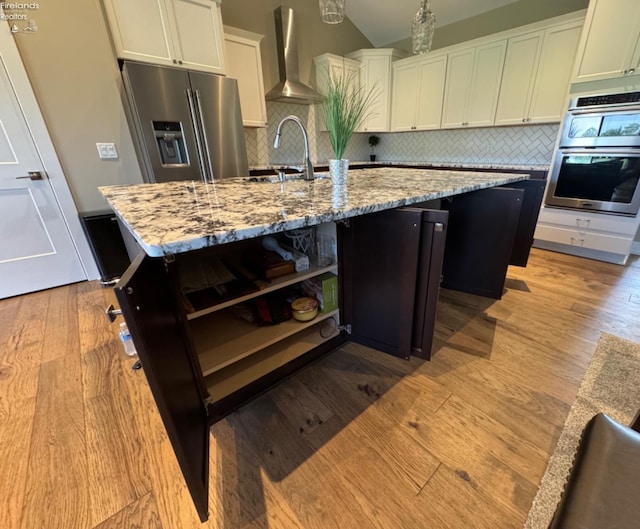 kitchen with open shelves, wall chimney range hood, light wood-type flooring, appliances with stainless steel finishes, and a sink