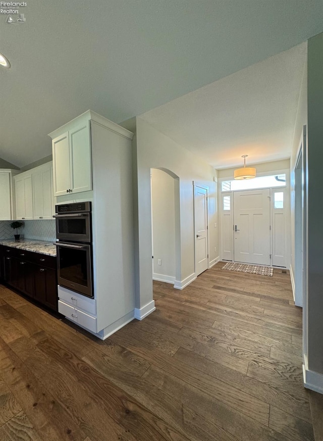 kitchen with double wall oven, dark wood finished floors, arched walkways, decorative backsplash, and baseboards