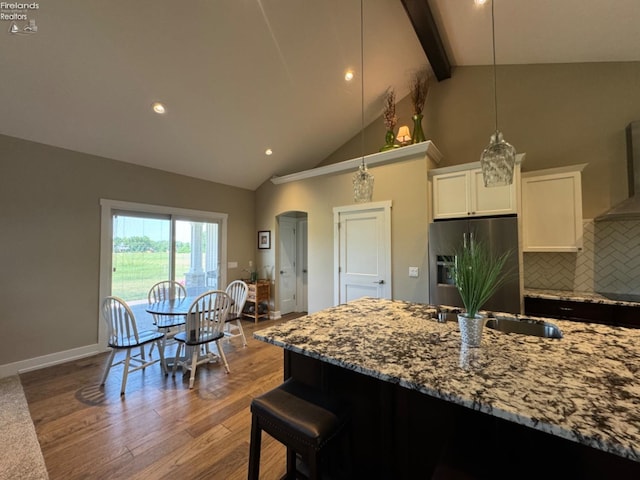 kitchen with dark wood finished floors, wall chimney exhaust hood, light stone countertops, and stainless steel refrigerator with ice dispenser