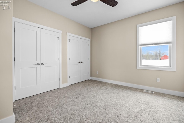 unfurnished bedroom featuring visible vents, carpet floors, baseboards, ceiling fan, and multiple closets