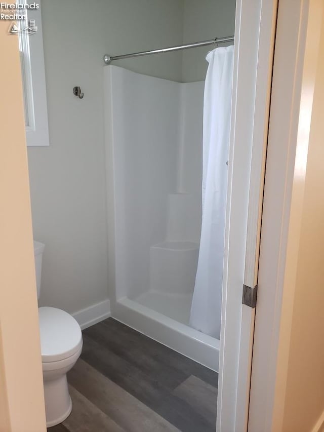 bathroom with toilet, a shower with shower curtain, baseboards, and wood finished floors