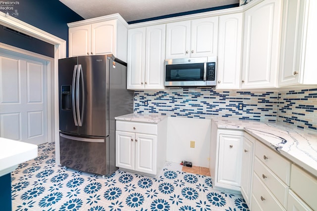 kitchen with a textured ceiling, stainless steel appliances, light stone countertops, and white cabinets