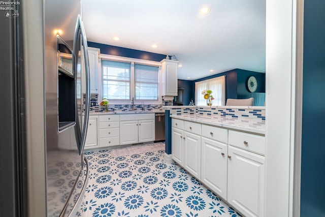 kitchen featuring appliances with stainless steel finishes, light stone counters, white cabinetry, kitchen peninsula, and tasteful backsplash