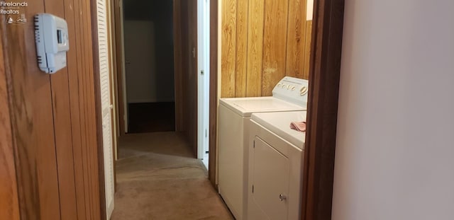 clothes washing area featuring separate washer and dryer, wood walls, and light colored carpet