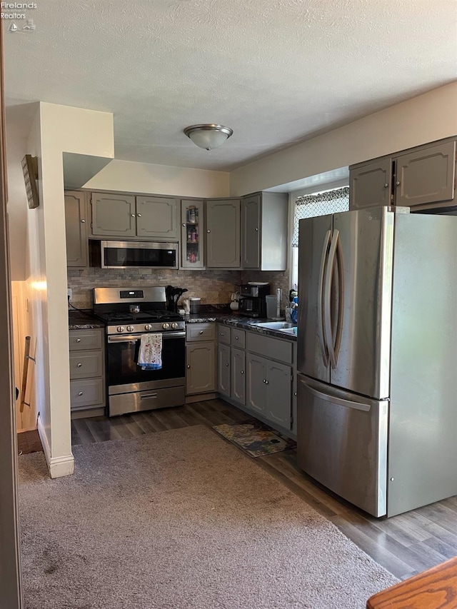 kitchen with appliances with stainless steel finishes, a textured ceiling, dark wood-type flooring, gray cabinets, and tasteful backsplash