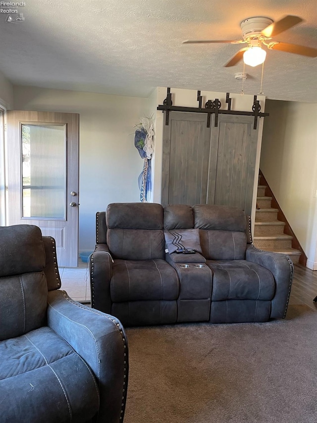 living room featuring a textured ceiling, carpet floors, ceiling fan, and a barn door