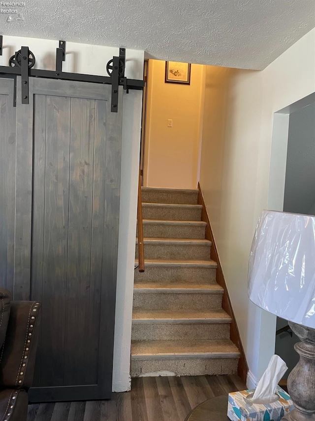 stairway featuring wood-type flooring, a barn door, and a textured ceiling