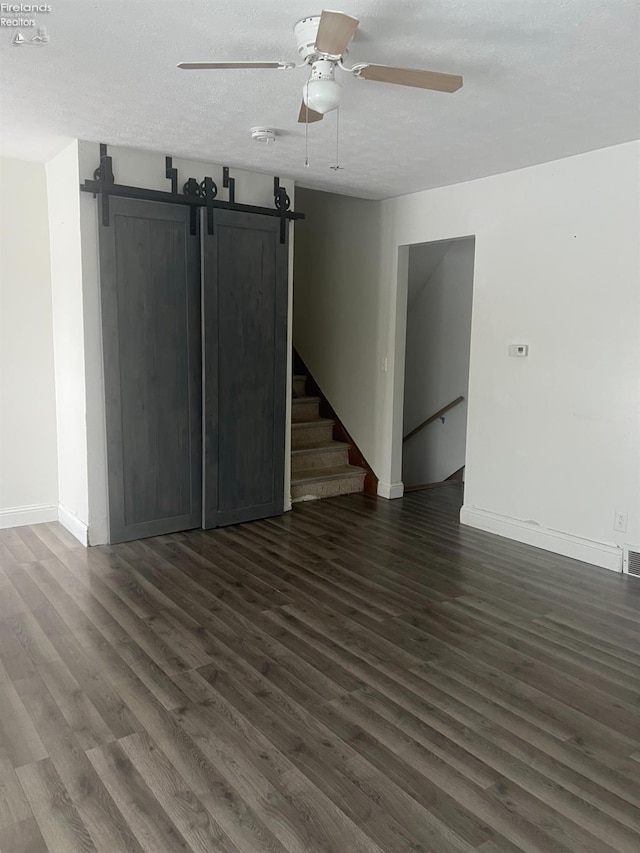 unfurnished living room featuring ceiling fan, dark wood-type flooring, a barn door, and a textured ceiling