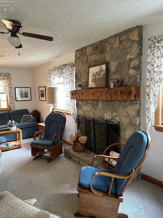 living room featuring a stone fireplace, a textured ceiling, ceiling fan, and carpet floors