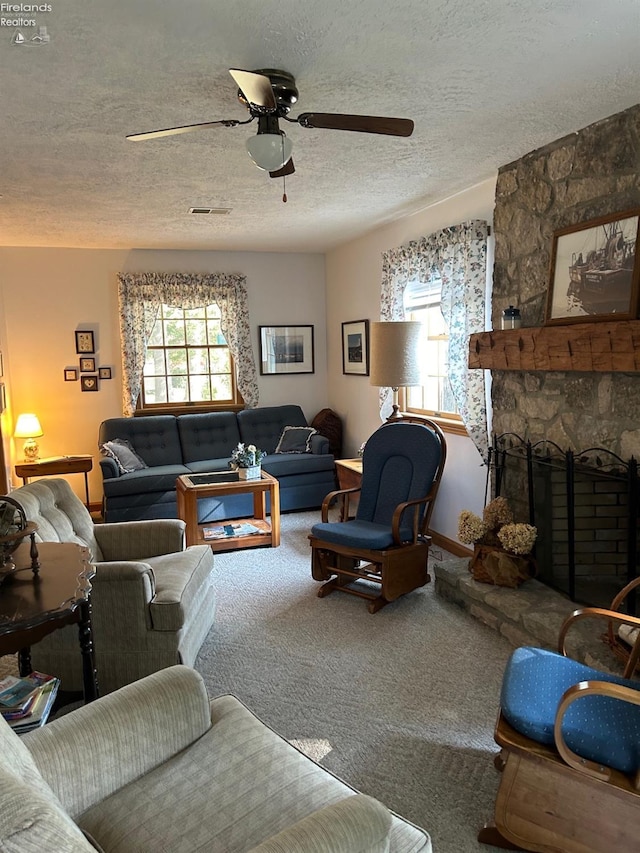 living room with visible vents, a ceiling fan, a textured ceiling, carpet floors, and a stone fireplace