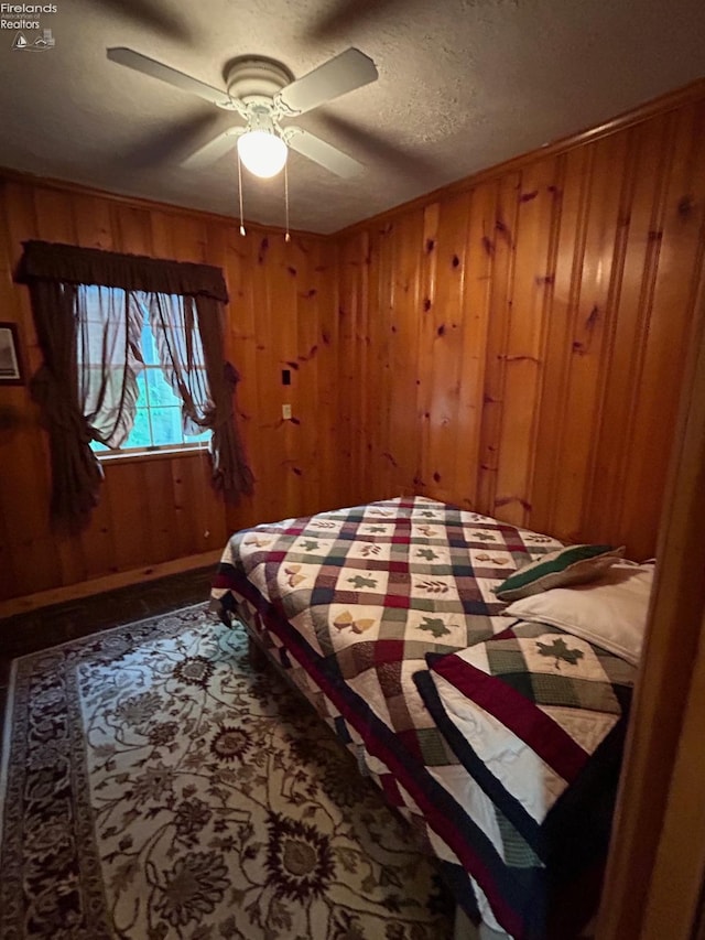 bedroom featuring baseboards, wooden walls, ceiling fan, and a textured ceiling