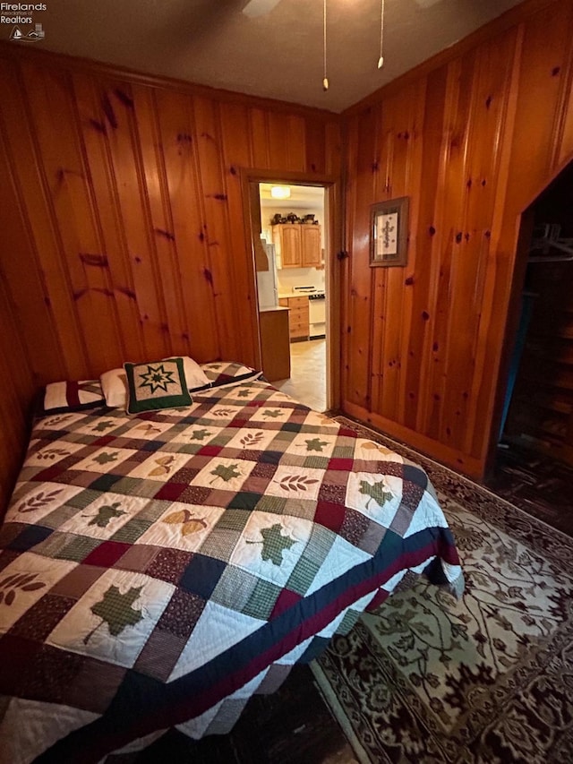 bedroom featuring wood walls and freestanding refrigerator