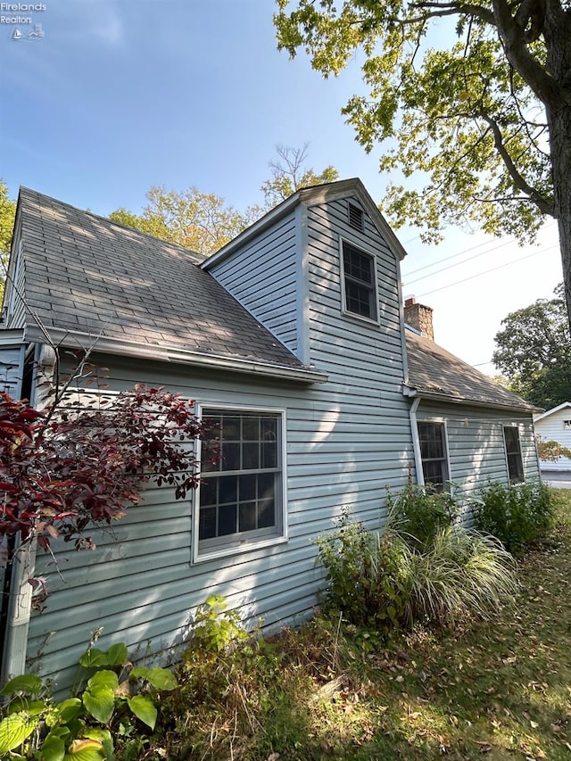 view of side of home with a chimney and a shingled roof