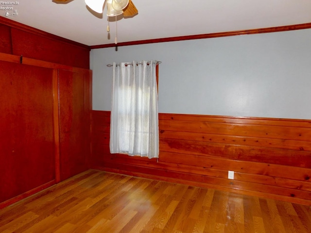 empty room featuring wood walls, ceiling fan, ornamental molding, and wood-type flooring