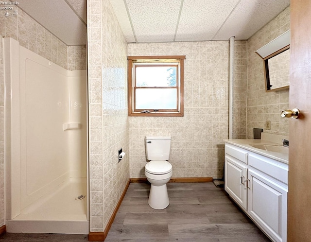 bathroom with hardwood / wood-style floors, walk in shower, toilet, tile walls, and vanity