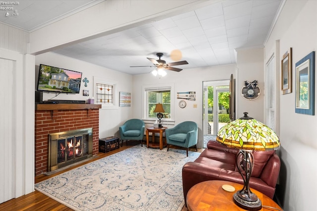 living room featuring ceiling fan, hardwood / wood-style flooring, crown molding, and a brick fireplace