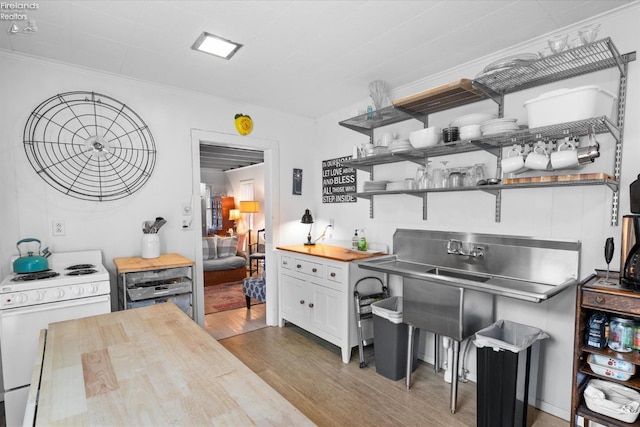 kitchen featuring white range with gas cooktop, wood-type flooring, ornamental molding, white cabinetry, and butcher block counters