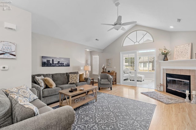 living room with light hardwood / wood-style flooring, ceiling fan, high vaulted ceiling, and a fireplace