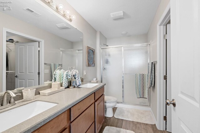 bathroom with hardwood / wood-style floors, toilet, a shower with door, and vanity