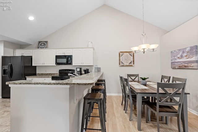 kitchen featuring pendant lighting, black appliances, kitchen peninsula, light stone countertops, and white cabinets