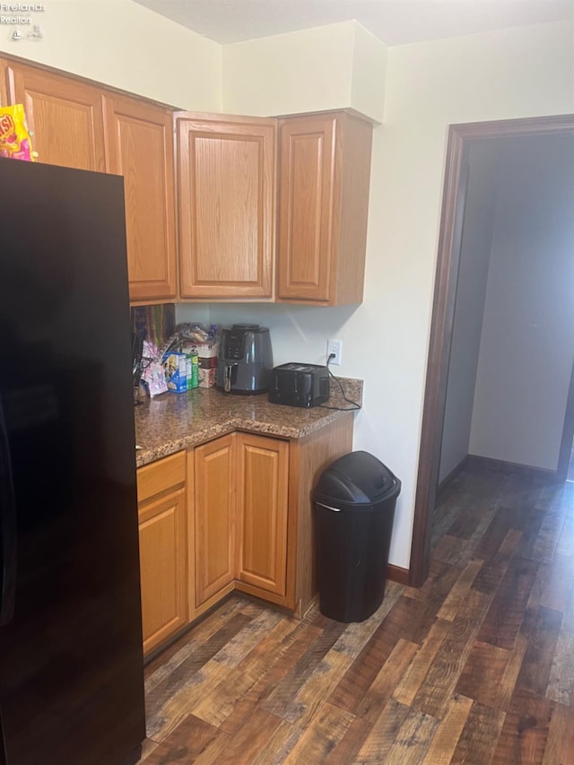 kitchen featuring dark stone countertops, black fridge, and dark wood-type flooring