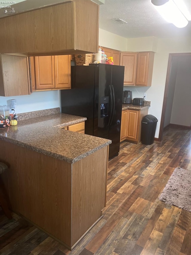 kitchen featuring kitchen peninsula, a textured ceiling, black fridge with ice dispenser, dark wood-type flooring, and dark stone countertops