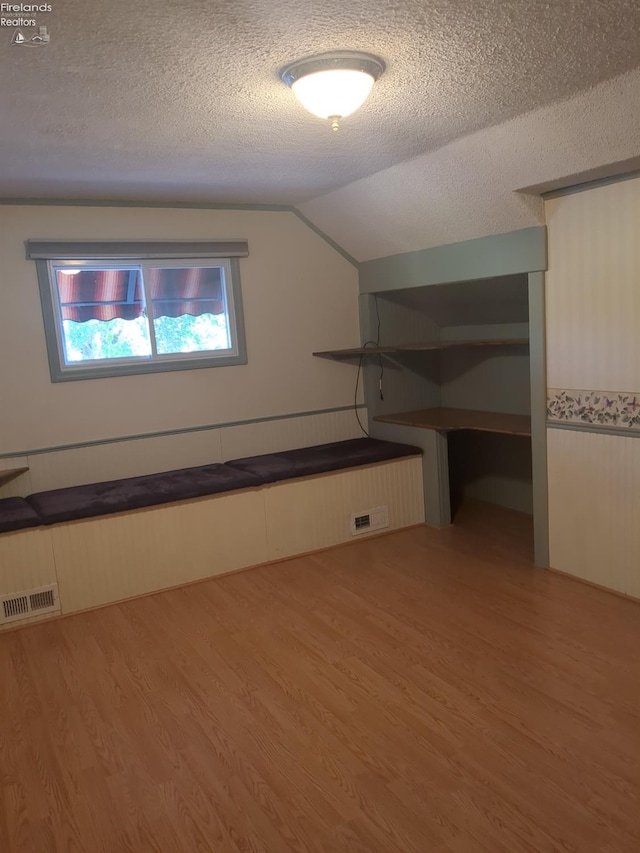 bonus room with a textured ceiling, light hardwood / wood-style flooring, and vaulted ceiling