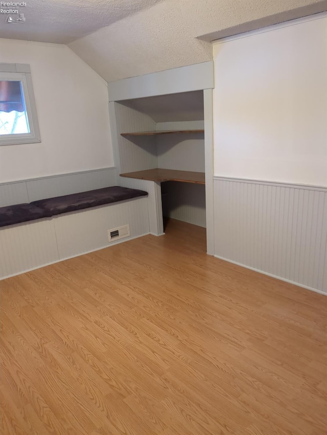 additional living space featuring light hardwood / wood-style floors, a textured ceiling, and vaulted ceiling