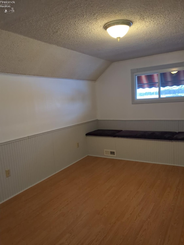 bonus room featuring a textured ceiling, hardwood / wood-style flooring, and lofted ceiling