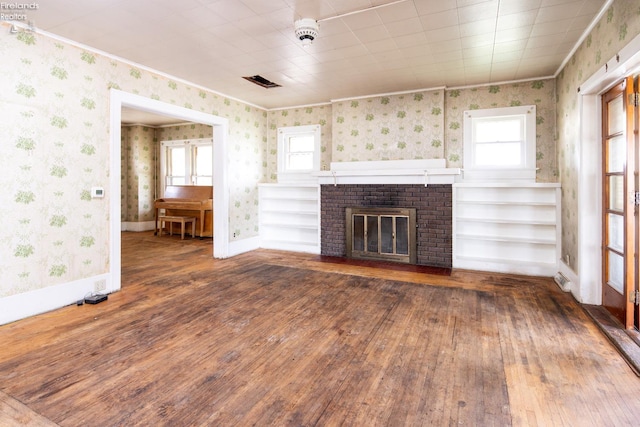 unfurnished living room with a brick fireplace, crown molding, dark wood-type flooring, and built in shelves