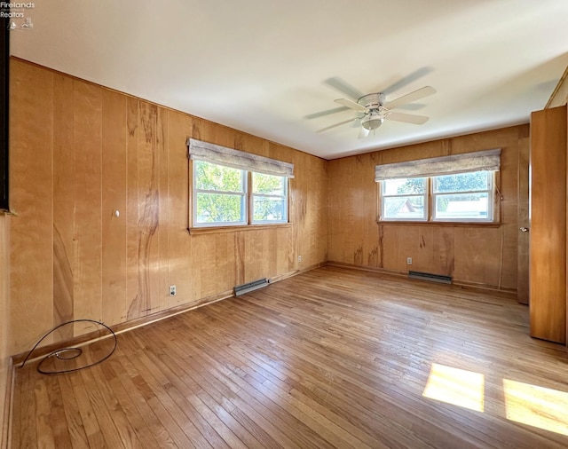 spare room with wooden walls, ceiling fan, light hardwood / wood-style flooring, and a wealth of natural light