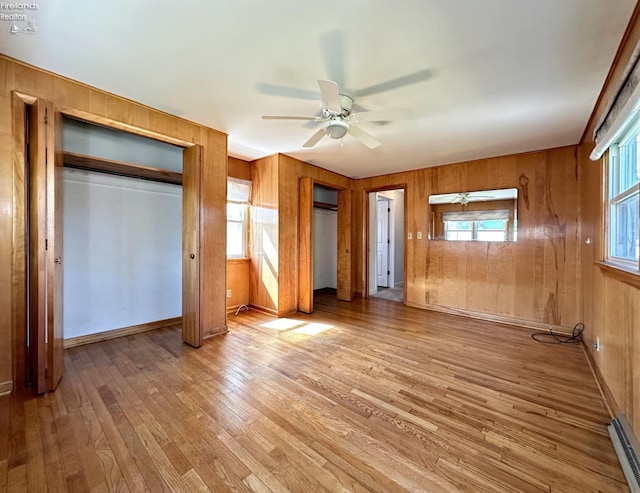 unfurnished bedroom featuring multiple windows, light hardwood / wood-style floors, wooden walls, and ceiling fan