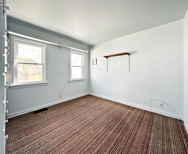 spare room featuring dark colored carpet and a wealth of natural light