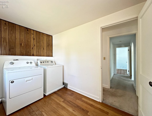 laundry room with wood walls, washer and dryer, and hardwood / wood-style flooring