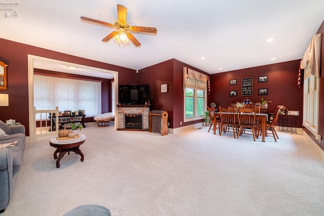 living room with ceiling fan, a stone fireplace, and light carpet