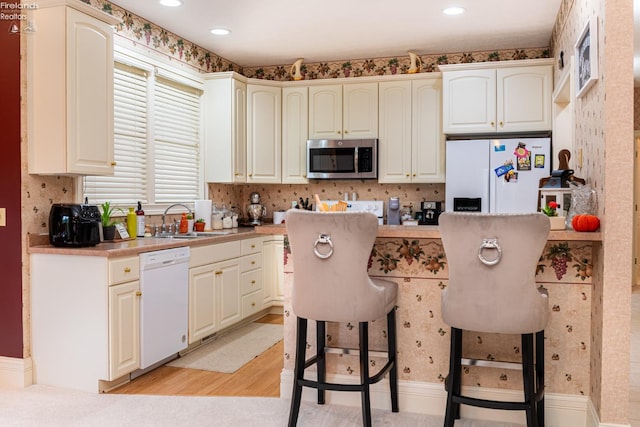 kitchen featuring a kitchen breakfast bar, white appliances, a kitchen island, light wood-type flooring, and sink