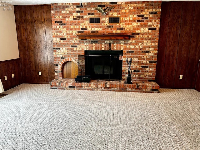 unfurnished living room featuring a brick fireplace, wooden walls, and carpet