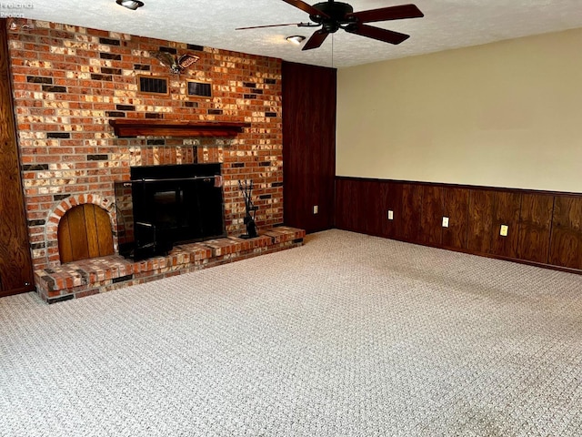 unfurnished living room featuring ceiling fan, a textured ceiling, a brick fireplace, and wood walls